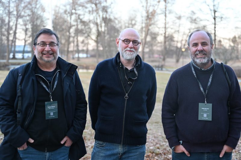 Three men outside, smiling.