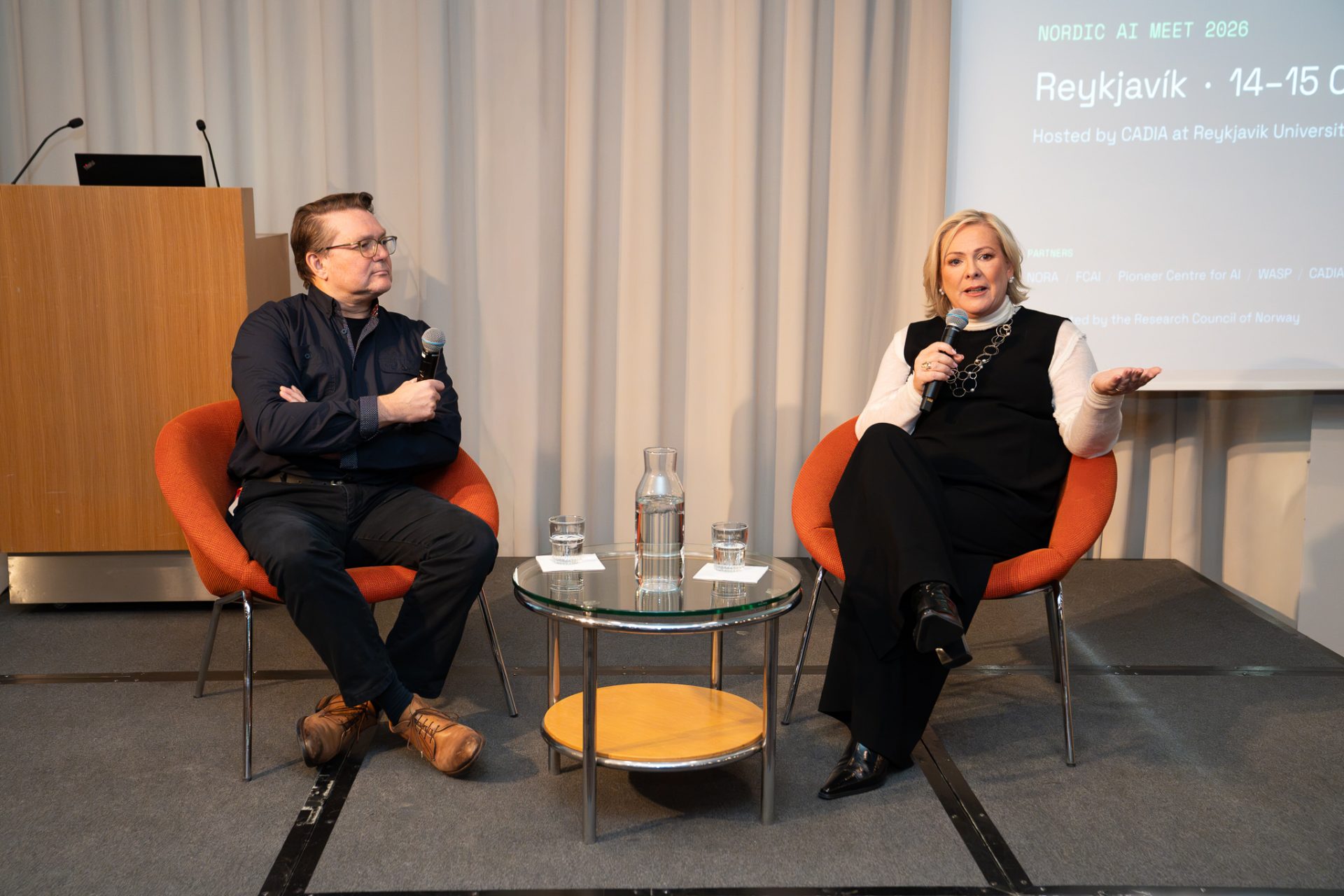 A man and women in chairs on a stage.