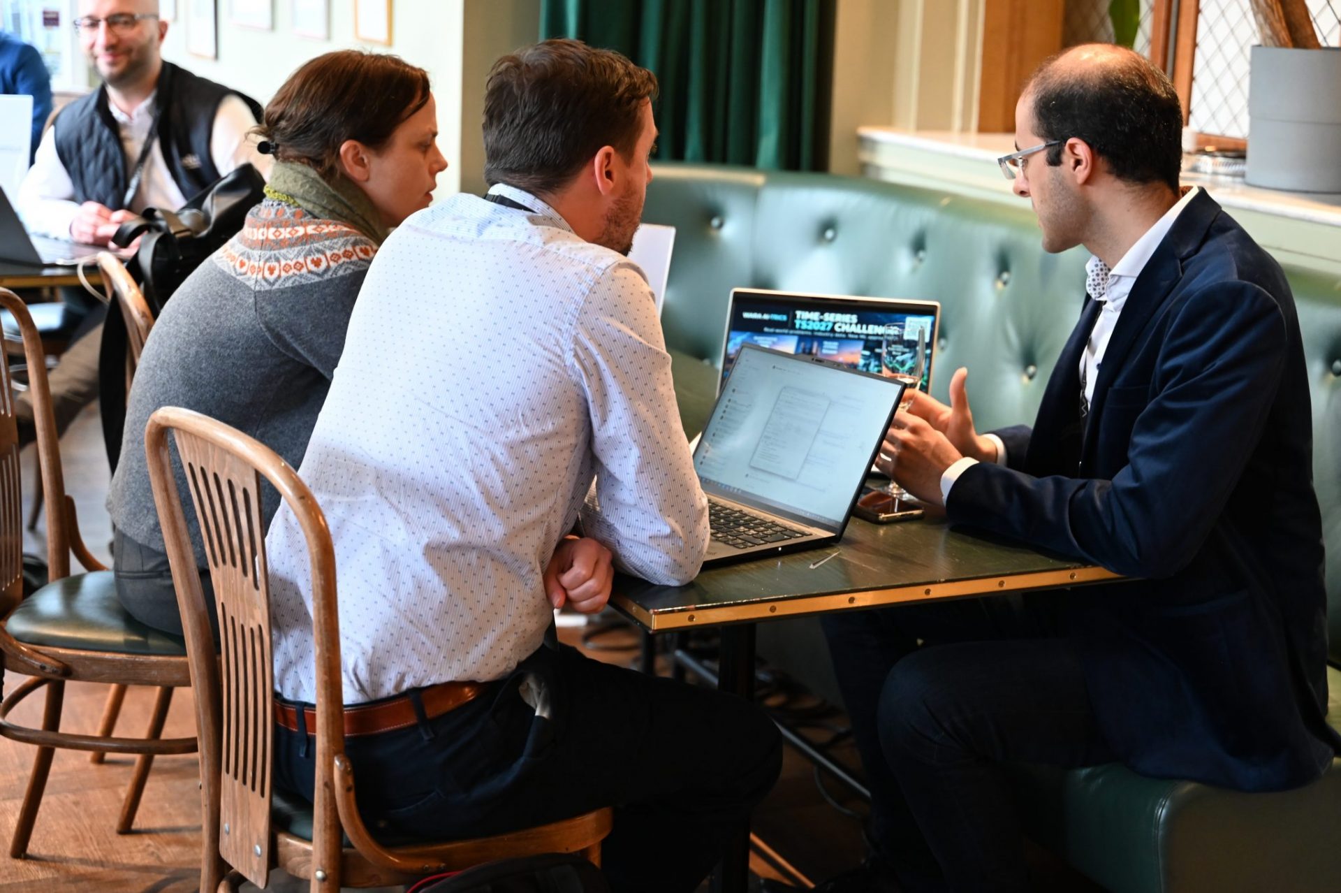 three men sitting by a table, looking at a computer
