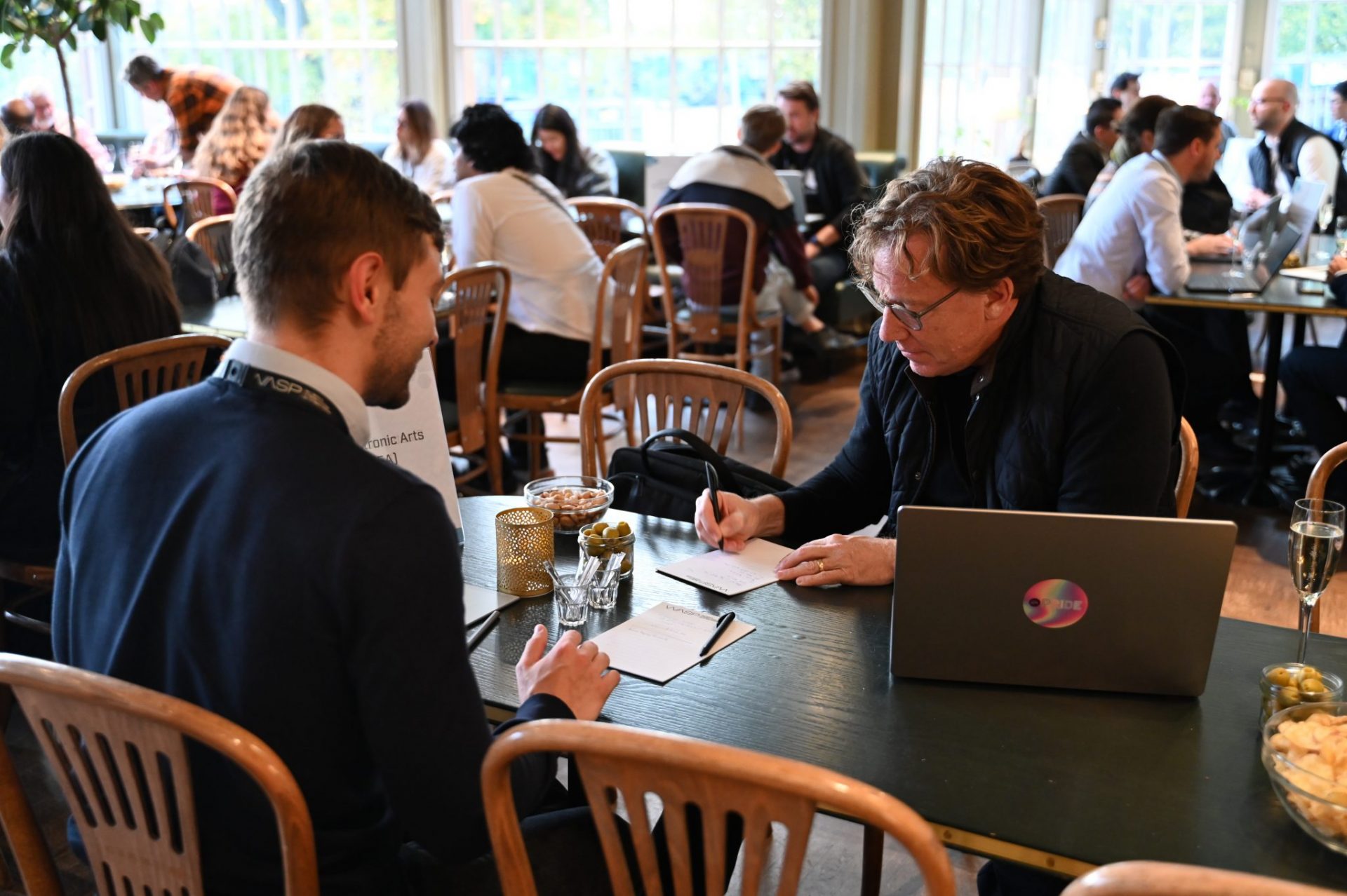 Two men sitting by a table, one is taking notes